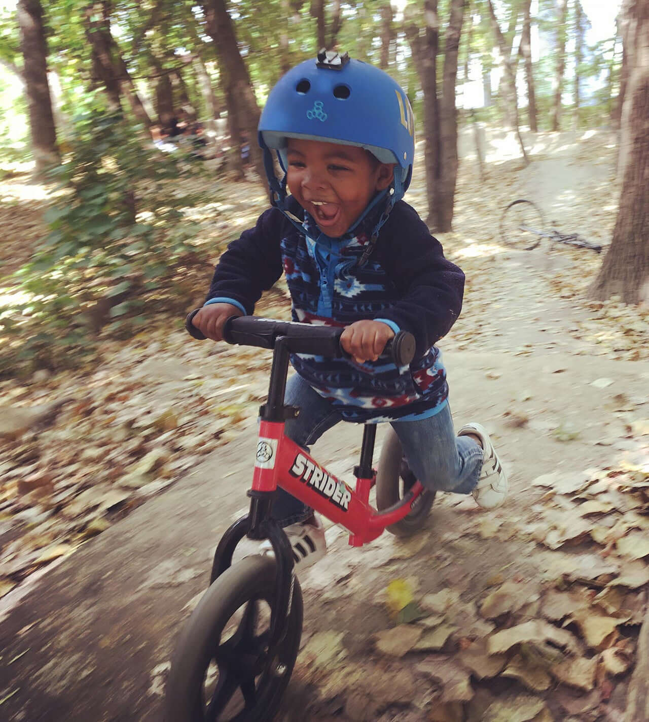 Child riding a Strider 12 Sport Balance Bike with a helmet, enjoying outdoor fun in a park.