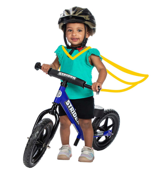 Toddler riding the Strider 12 Sport Balance Bike, wearing a helmet and colorful cape, ready for adventure.