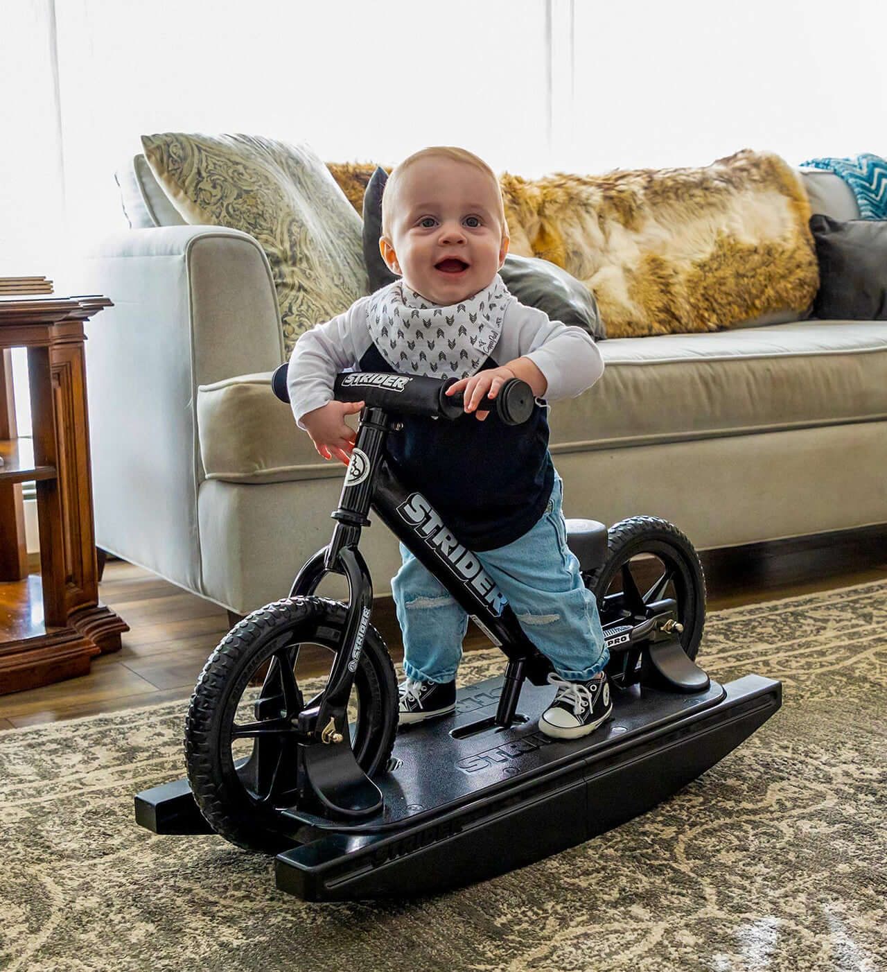 Happy baby riding the Strider Pro 2-in-1 Rocking Bike on a rocking base indoors.