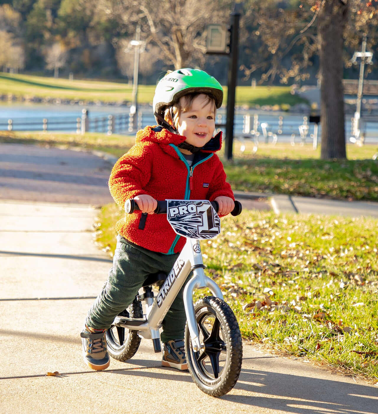 Young child riding the Strider 12 Pro Balance Bike on a sunny day, showcasing joy and adventure in a park setting.