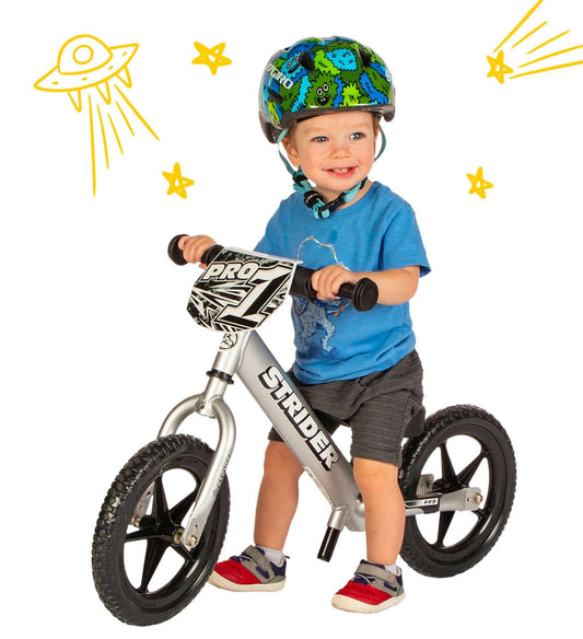 Child riding the Strider 12 Pro Balance Bike with a helmet, smiling and ready for adventure.