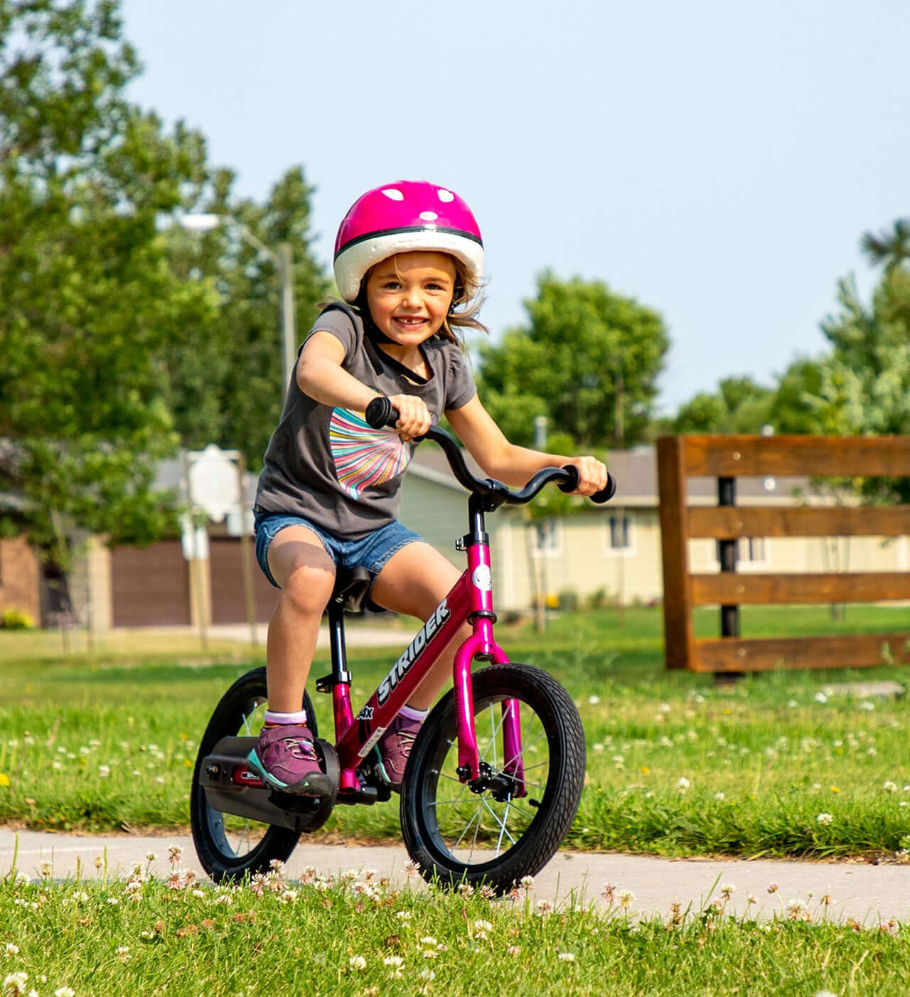 Young girl riding the Strider 14x Convertible Bike with helmet in a grassy park setting.