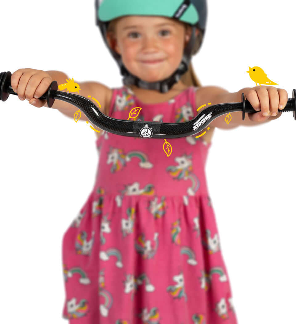 Girl smiling while holding Strider Carbon Fiber Riser Handlebar, wearing a helmet and a colorful unicorn dress.