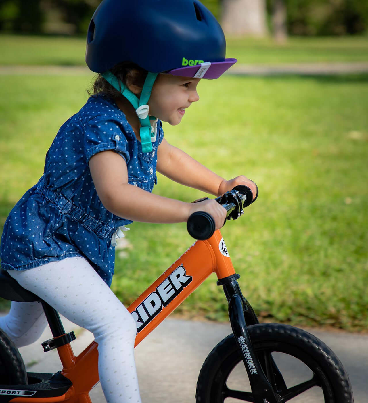 Child riding a Strider balance bike, wearing a helmet and smiling while enjoying outdoor fun.