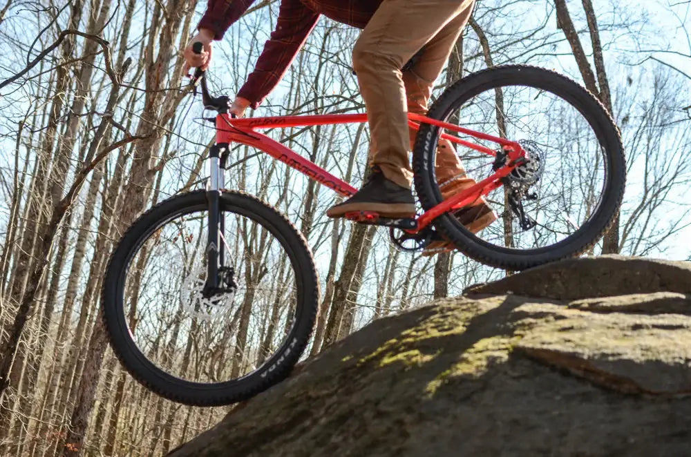 A rider skillfully maneuvers the Eastern Bike Alpaka 27.5" over a rocky terrain, showcasing its agility and design.