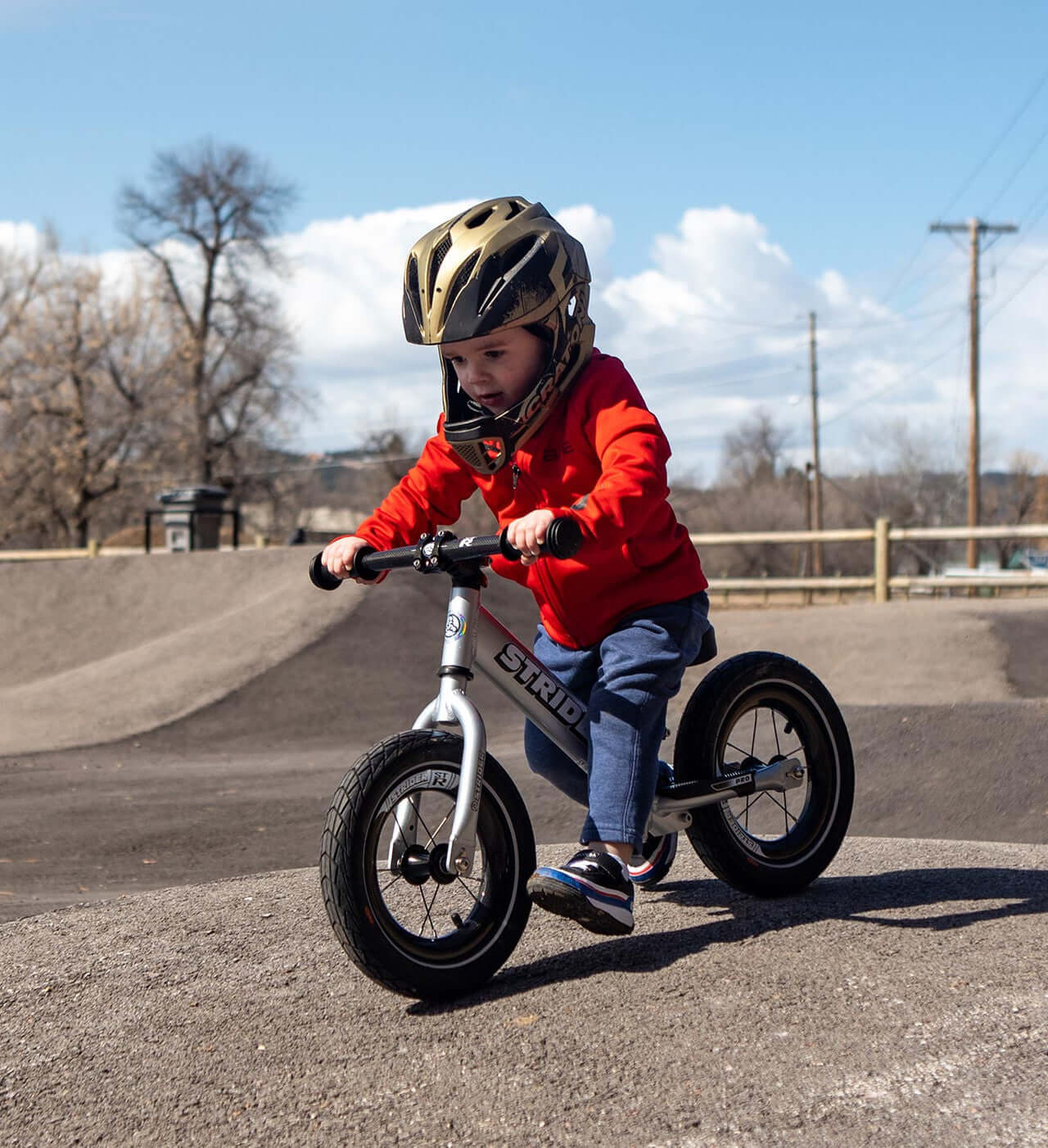 Child riding a Strider balance bike with carbon fiber wheels, demonstrating speed and agility on a sunny day.