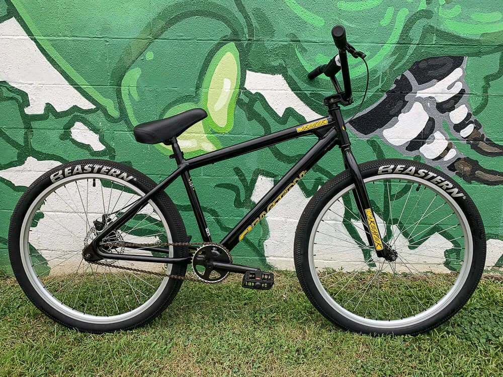 Eastern Bike Big Reaper LTD in black against a vibrant green mural, showcasing its 26" wheels and sleek design.