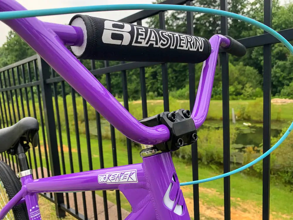 Close-up of the Eastern Big Reaper LTD bike handlebars and grips, showcasing its vibrant purple color and design.