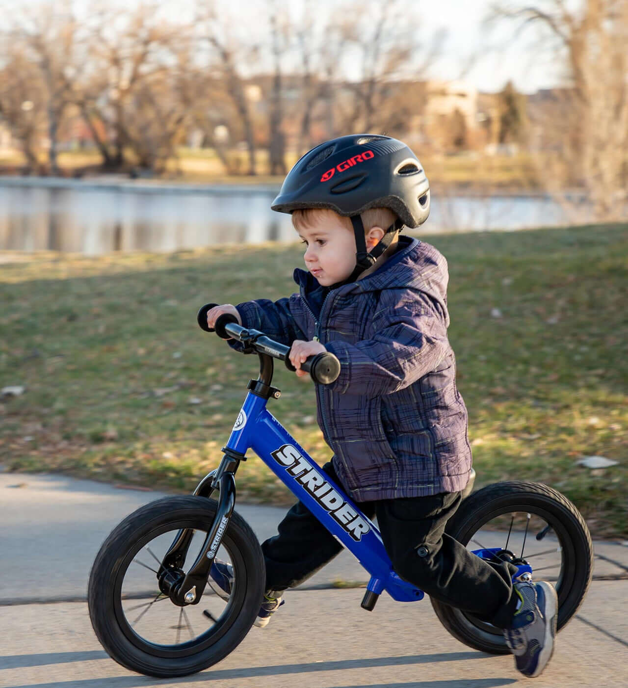 Child riding a Strider balance bike with high-traction wheels near a lake, showcasing outdoor fun and safety.
