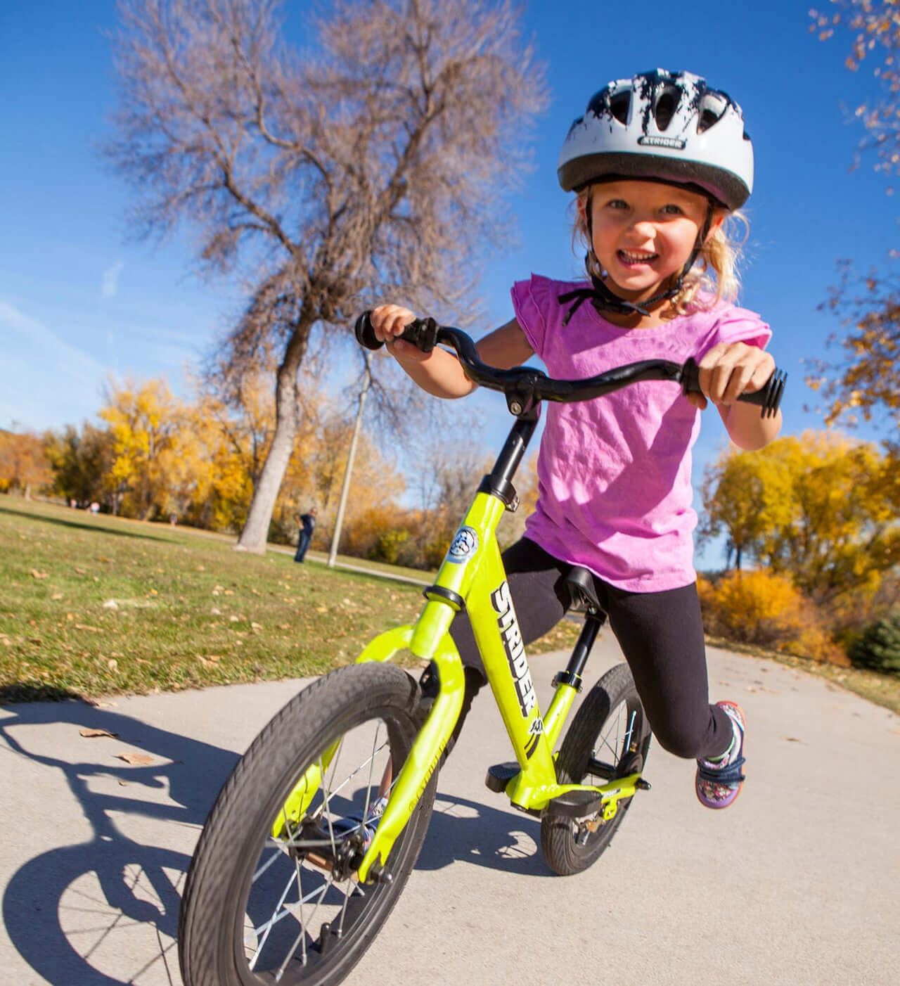 Happy child riding a Strider bike wearing a splash design helmet in a sunny park.