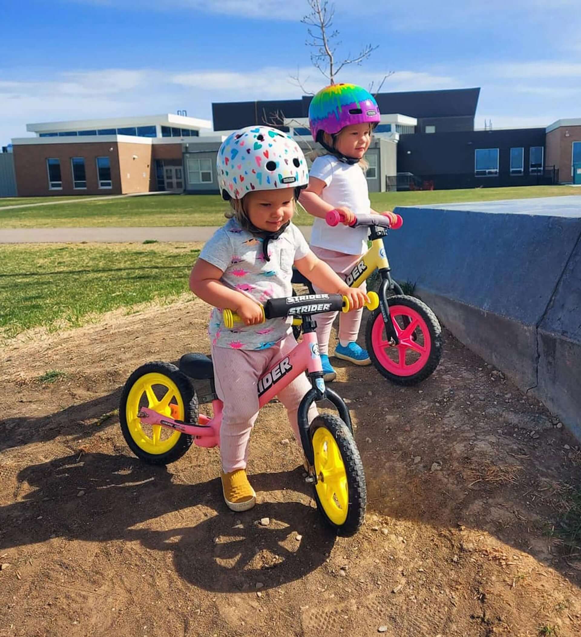 Two kids riding Strider balance bikes with colorful Ultralight Wheels in a park.